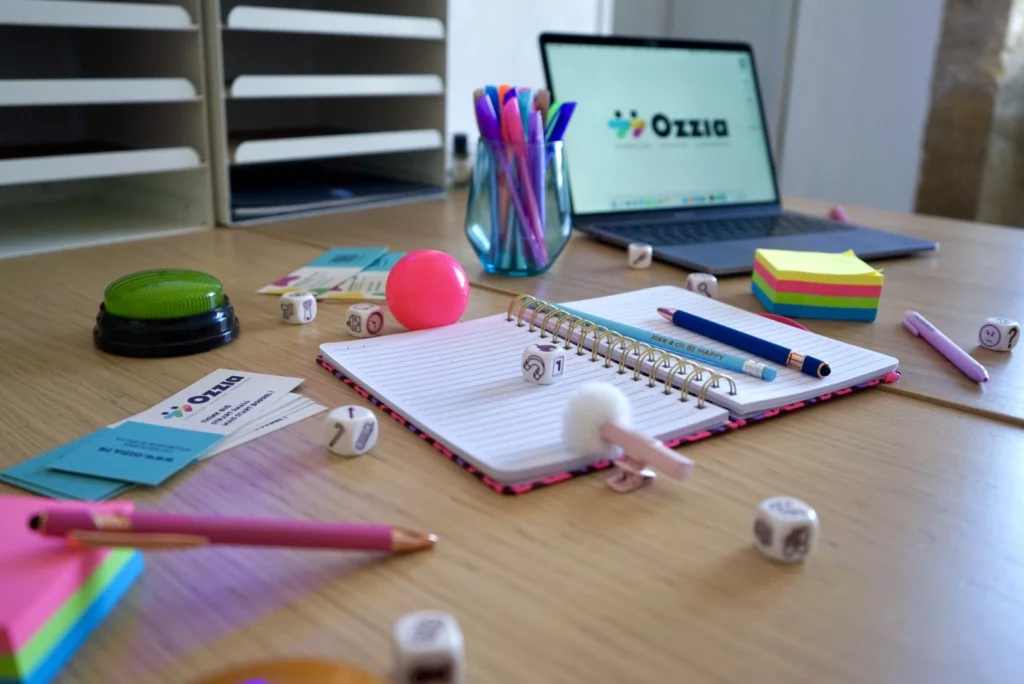 Vue plongeante sur un bureau sur lequel sont disposés des accessoires colorés utilisés pendant les formations : stylos, carnet, dés, postit, ...