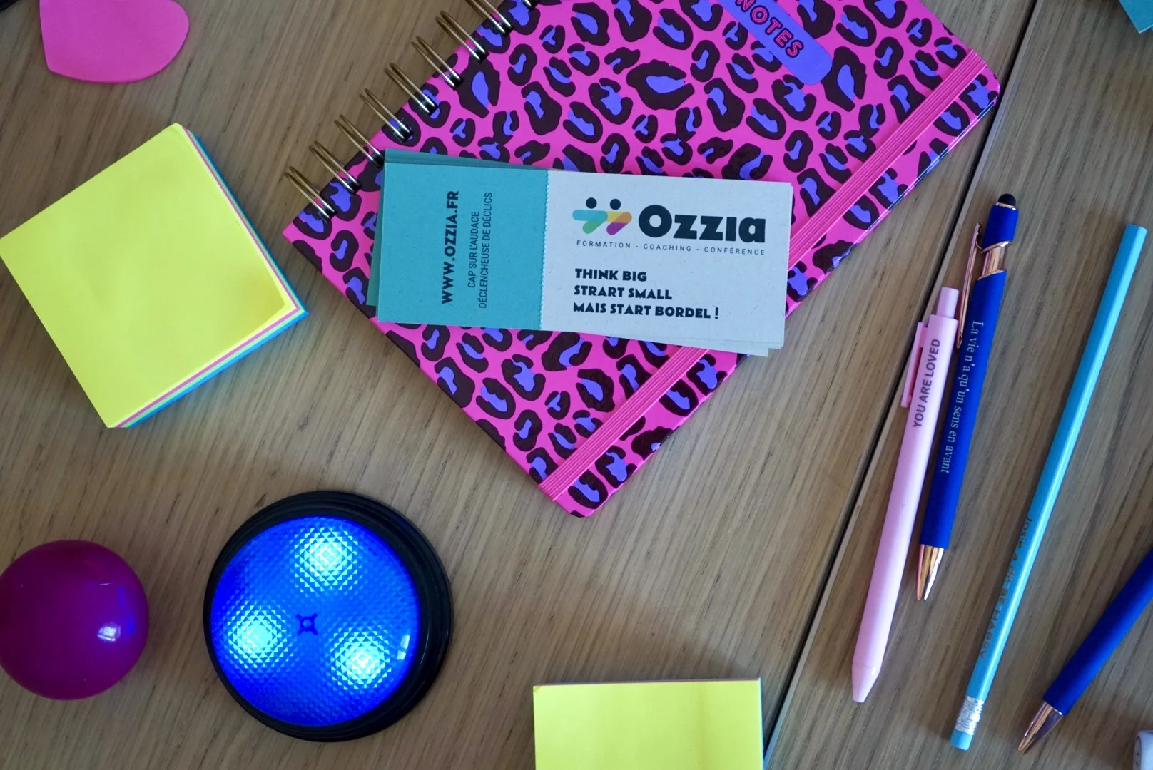 Objets de bureau colorés (carnet, stylos, buzzer, ...) déposés sur une table pour illustrer les formations Ozzia